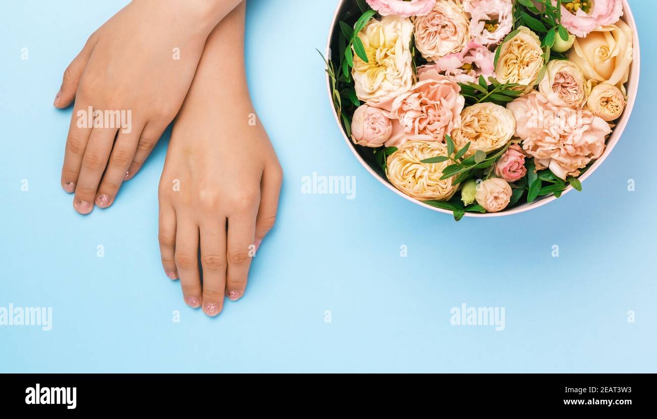 Boîte avec de belles fleurs à côté des mains de womans sur le fond bleu avec espace de copie. Concept de carte salone beauté. Cadeau pour le 8 mars, Fête des mères Banque D'Images