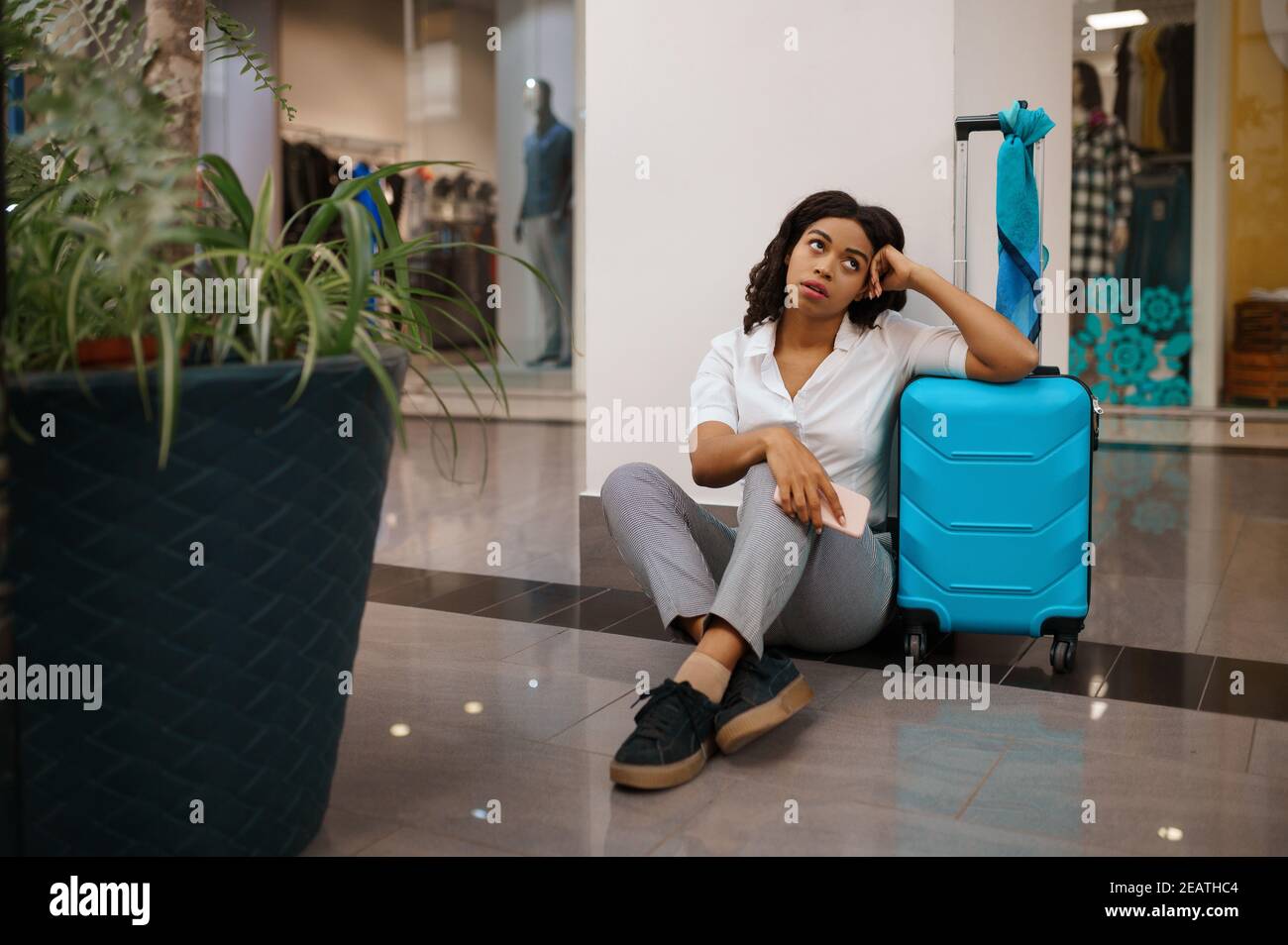 Femme avec une valise assise sur le sol, à l'aéroport Banque D'Images