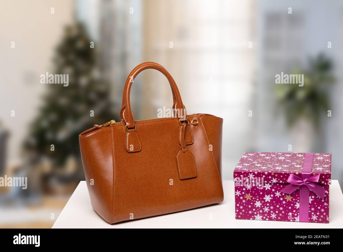 Modèle pour les soldes de noël. Élégant sac à main de luxe marron féminin  et boîte cadeau sur la table avec un arrière-plan d'arbre de Noël flou à  l'intérieur. Publicité accessoires femme