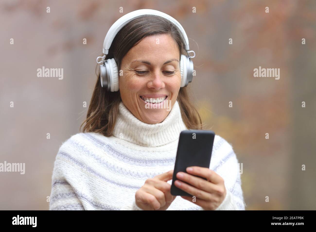 Bonne femme d'âge moyen écoutant de la musique sur le téléphone Banque D'Images