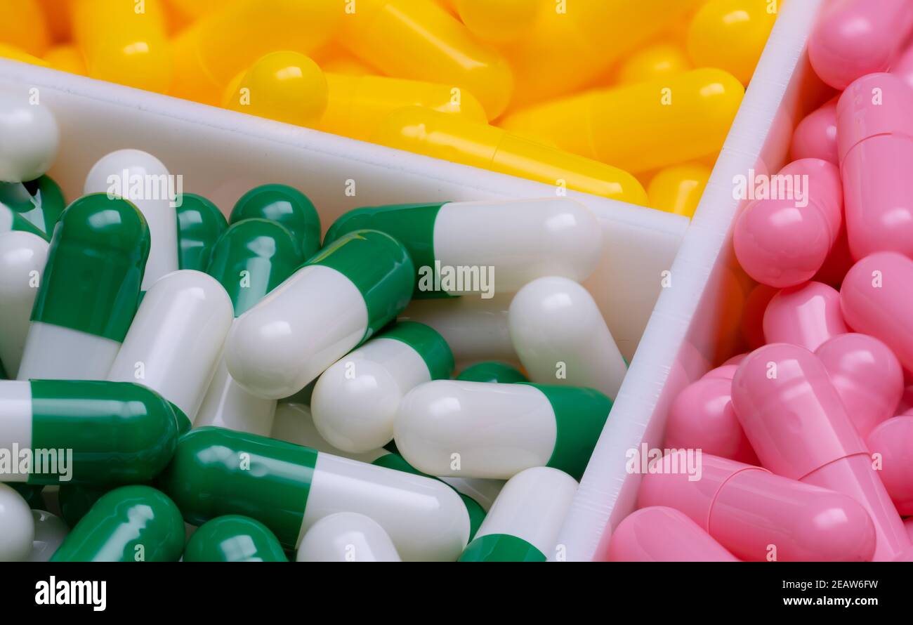 Pilules de capsule rose et vert-blanc sur les pilules de capsule jaune de flou dans une boîte en plastique. Vitamines et suppléments concept. Industrie pharmaceutique. Produits pharmaceutiques dans le plateau de médicaments Banque D'Images