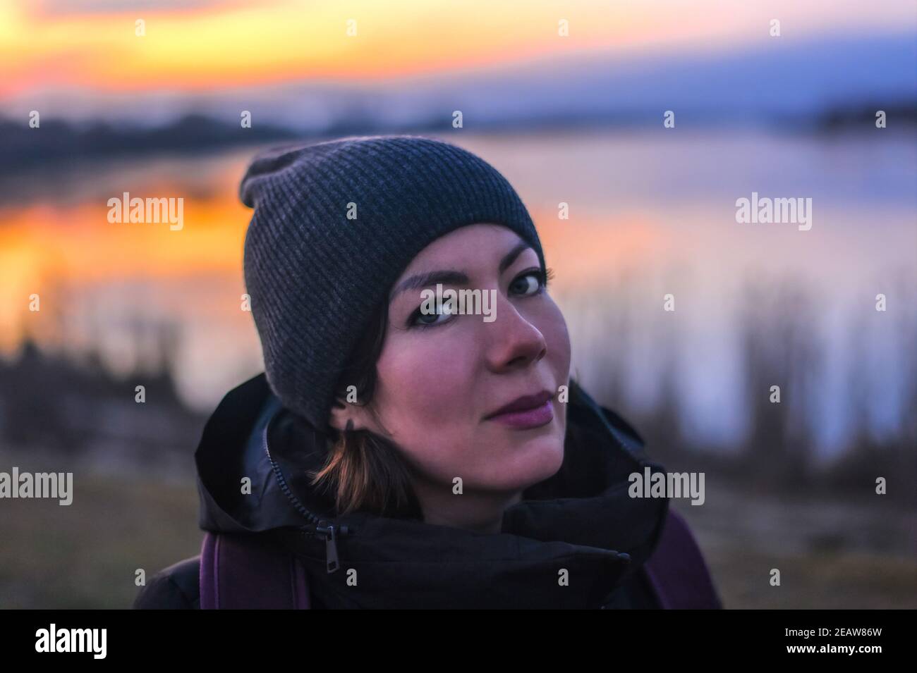 Portrait d'une belle jeune femme dans une casquette en tricot et vêtements d'hiver sur le lac au coucher du soleil Banque D'Images