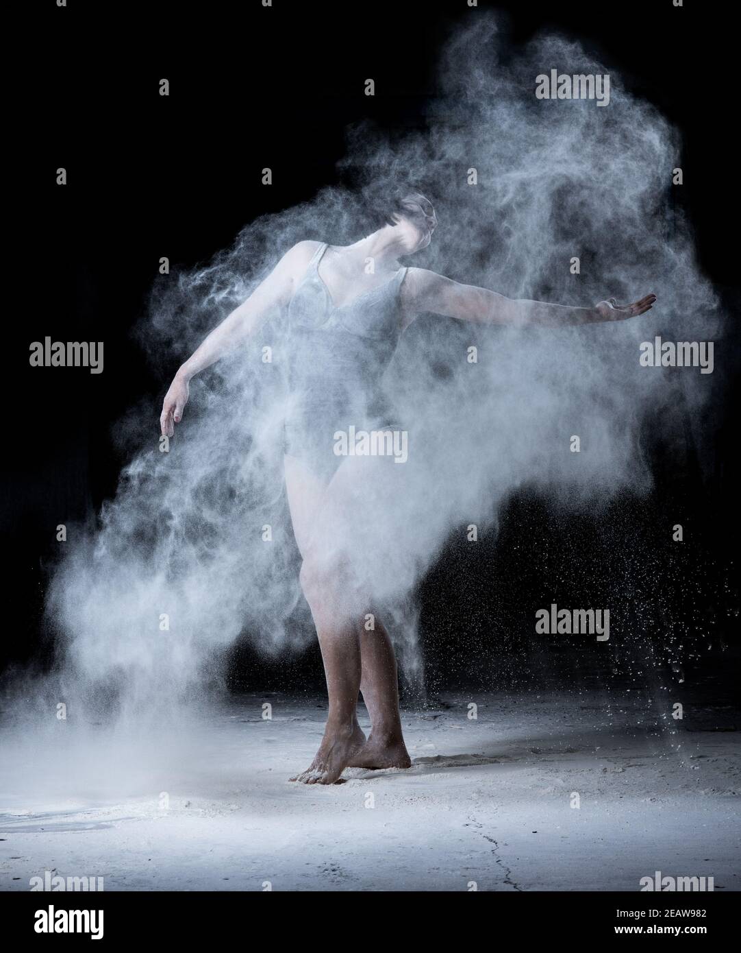 femme avec une figure sportive dansant dans un nuage de farine blanche dispersée sur fond noir Banque D'Images
