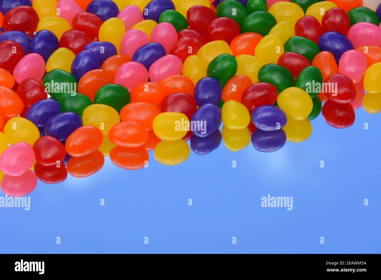 Des jelly beans colorés sur le miroir avec le reflet du ciel bleu de fond. Copier l'espace. Pour une utilisation en arrière-plan. 3 dimensions. Banque D'Images