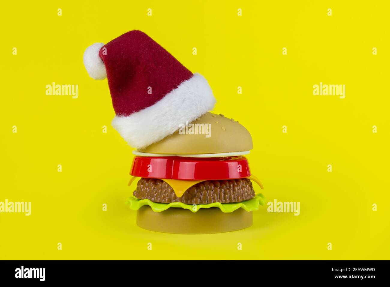 Chapeau de père Noël avec hamburger sur fond jaune. Restauration rapide Christmass. Hamburger enveloppé de cadeau. Concept de nourriture artificielle nocive Banque D'Images