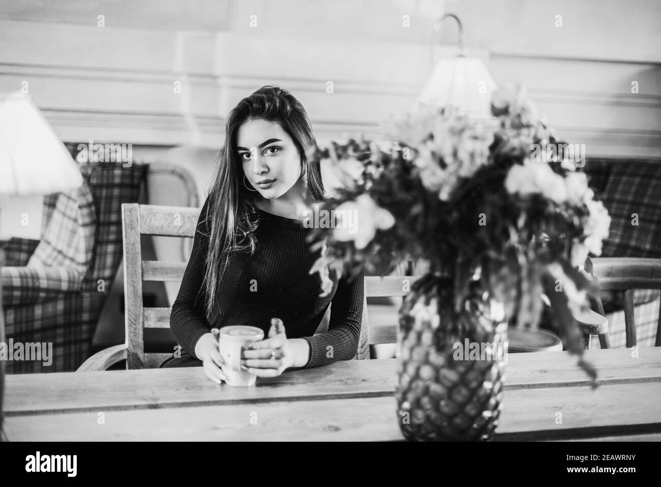 Belle femme avec une tasse de thé ou de café. Photographie en noir et blanc d'une fille dans un café. Brunette Banque D'Images