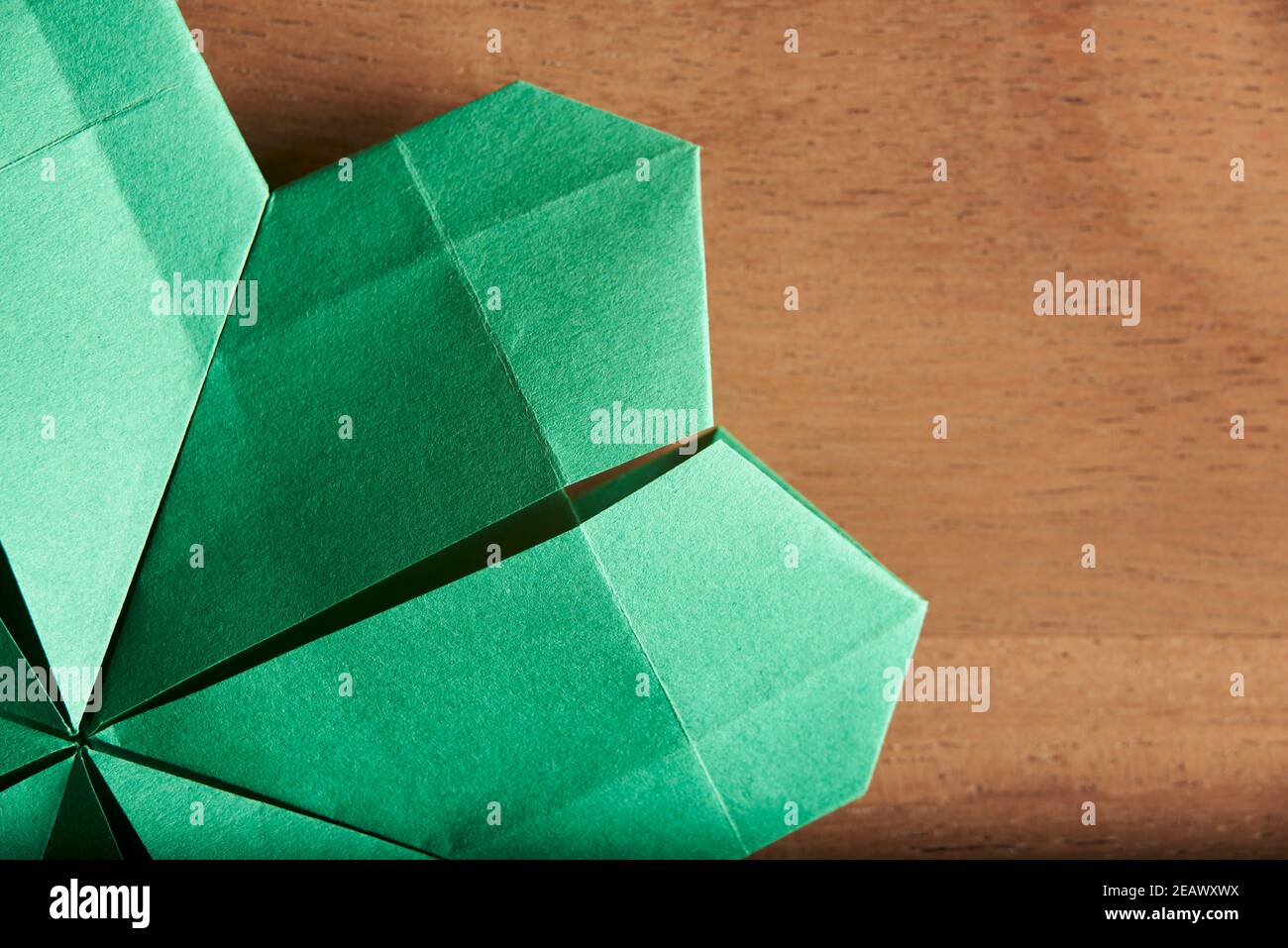 Détail d'un trèfle à quatre feuilles en papier vert plié suivant la technique de l'origami, sur fond de bois. Flat lay, gros plan. Banque D'Images