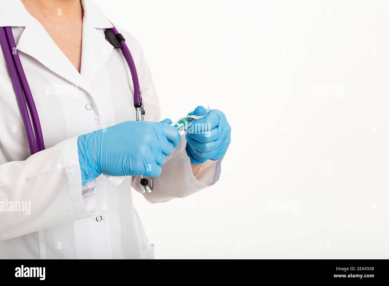 Une jeune infirmière dans un masque ouvre une seringue sur un fond blanc dans un manteau blanc, pour faire une vaccination, une injection. Le concept de vaccination et Banque D'Images