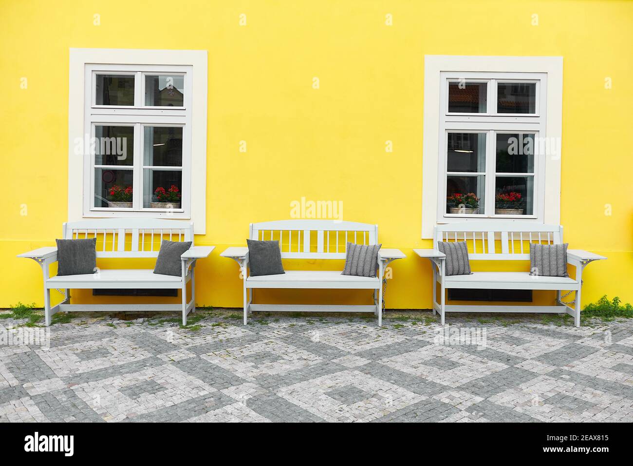 Prague à la mode. Maison peinte jaune lumineuse avec façade classique et trois bancs en bois blanc debout par deux fenêtres blanches. Banque D'Images
