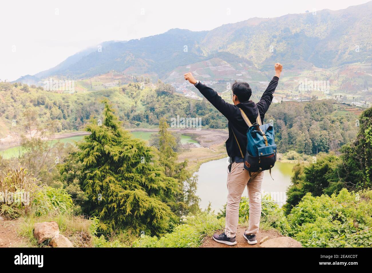 Jeune homme debout sur un rocher d'une falaise et profitant de la vue sur la nature du lac et de la montagne à Dieng Indonésie. Banque D'Images