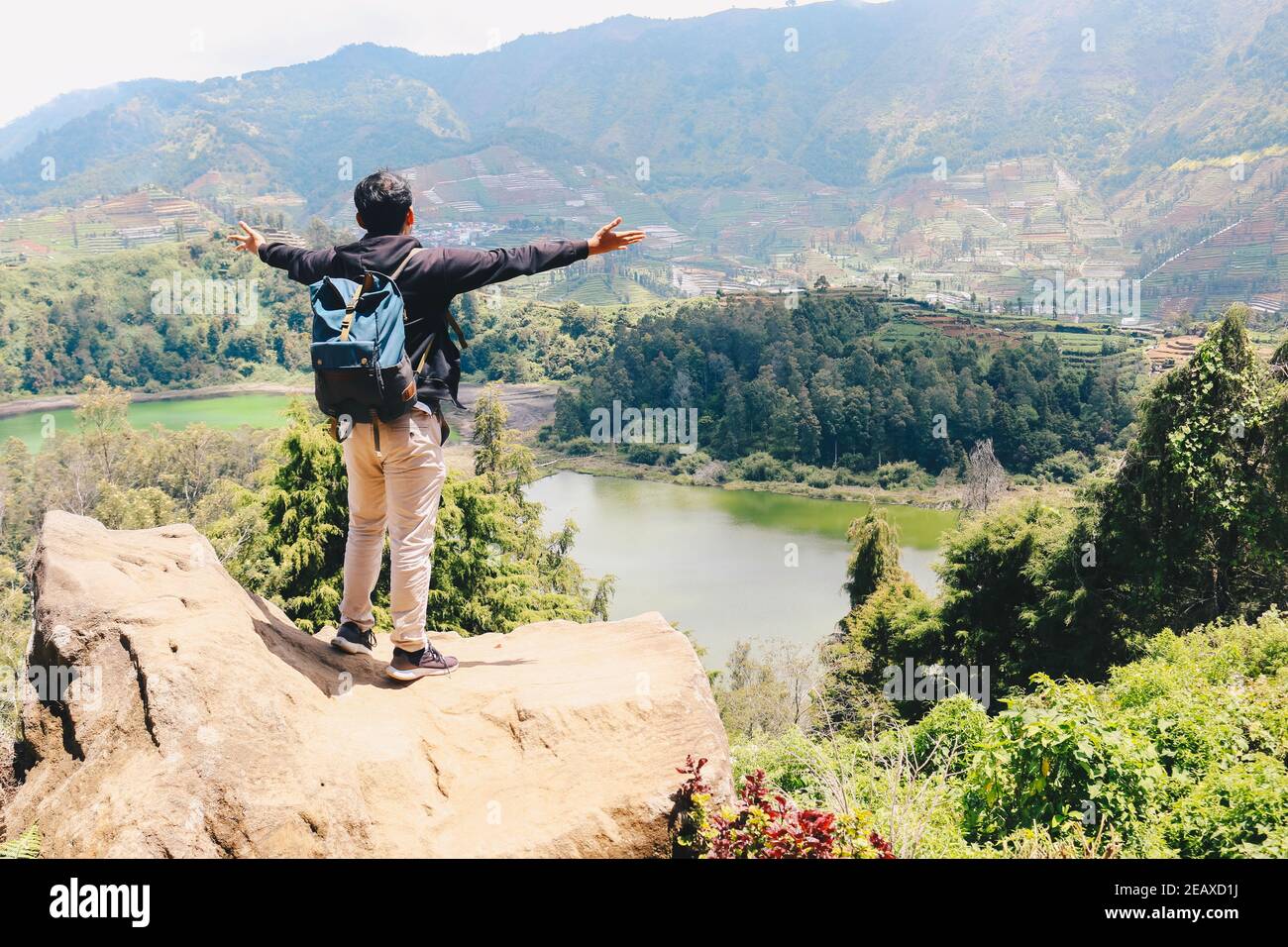 Jeune homme debout sur un rocher d'une falaise et profitant de la vue sur la nature du lac et de la montagne à Dieng Indonésie. Banque D'Images