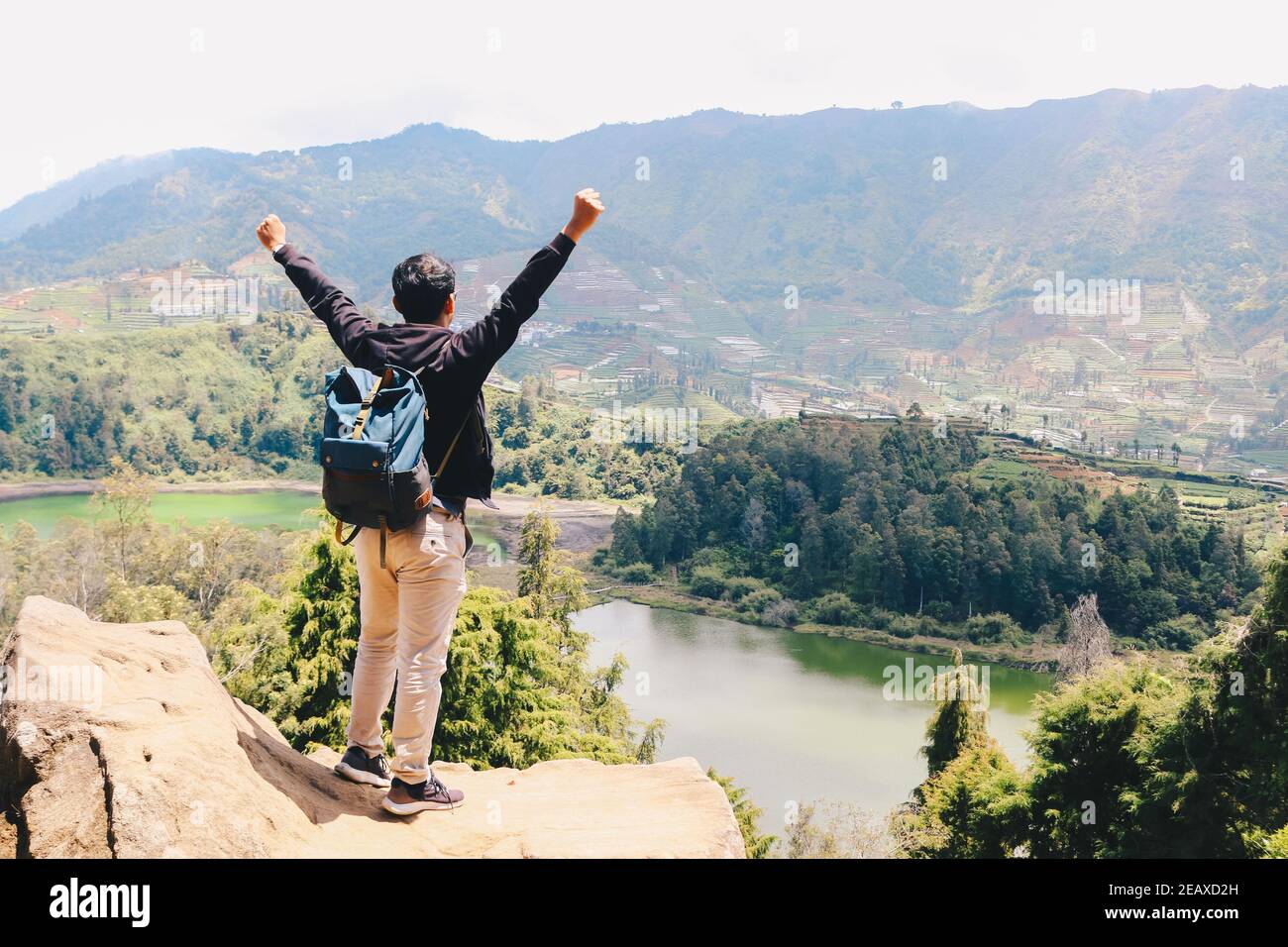 Jeune homme debout sur un rocher d'une falaise et profitant de la vue sur la nature du lac et de la montagne à Dieng Indonésie. Banque D'Images