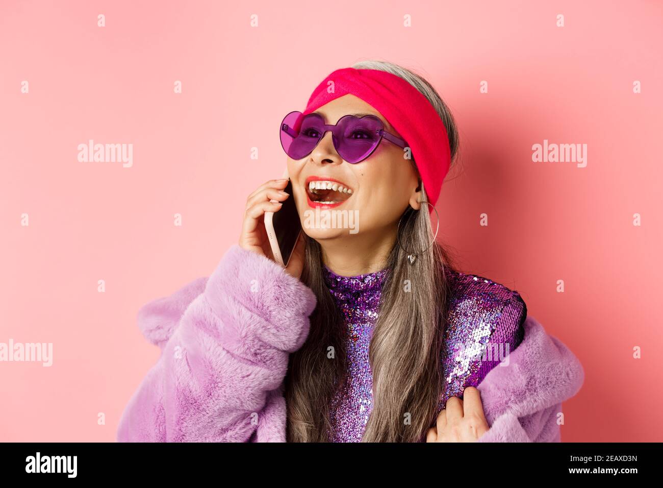 Mode. Belle femme asiatique senior dans des lunettes de soleil et serre-tête  tendance riant, parlant sur téléphone mobile et regardant de côté, fond  rose Photo Stock - Alamy