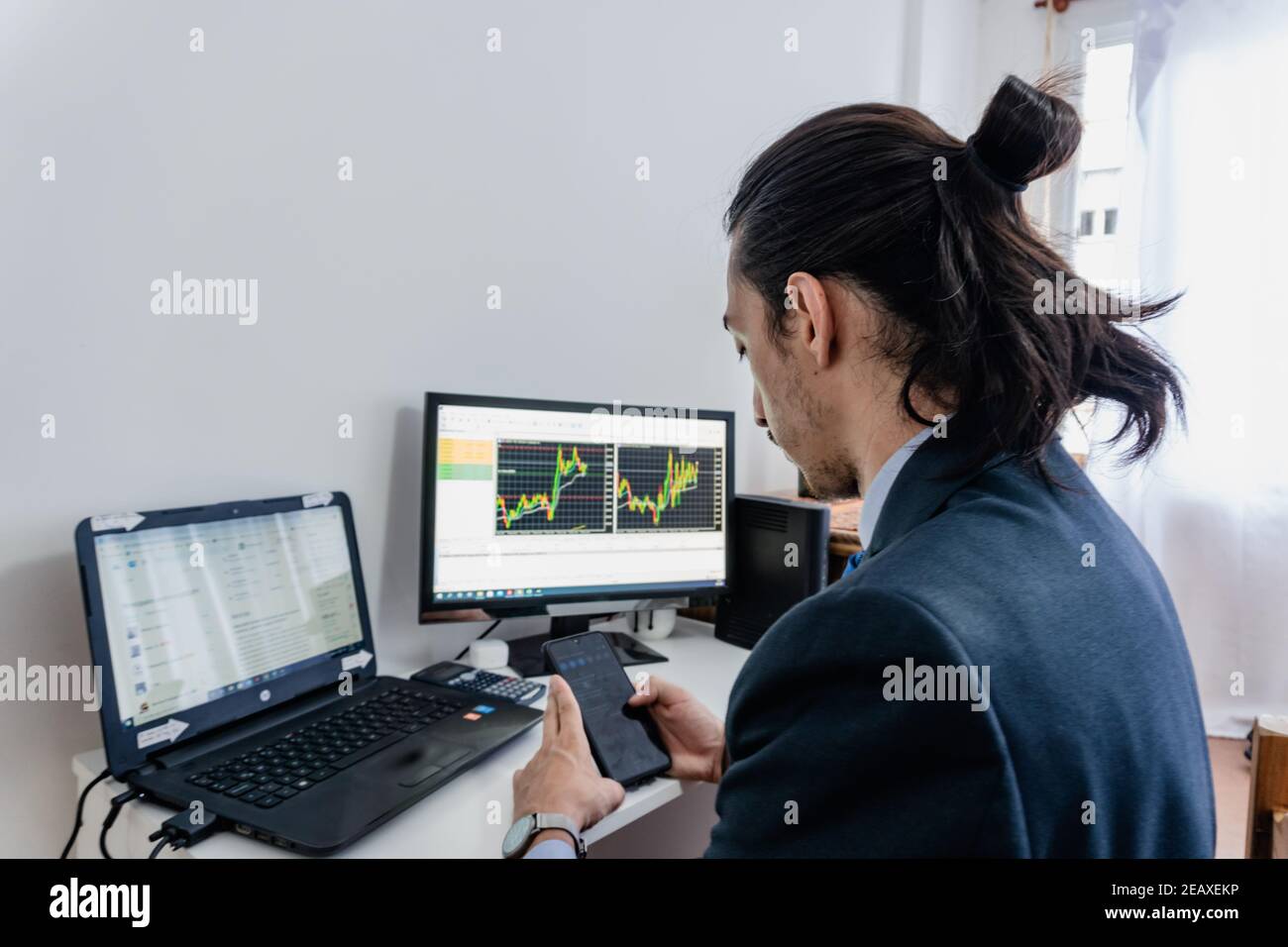 Un homme d'affaires à long terme qui investit dans la Bourse, regarde des graphiques sur deux ordinateurs et un téléphone portable, portant un costume bleu, Labor Day Banque D'Images