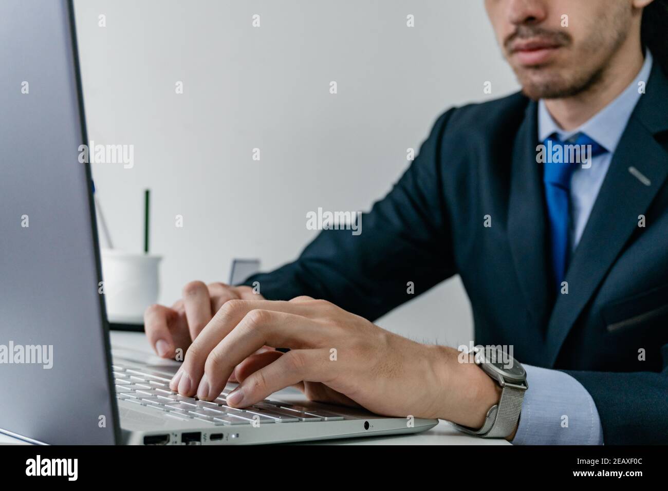 un jeune homme d'affaires tape sur un ordinateur portable moderne, portant un costume bleu monochrome avec une montre en titane, workday Banque D'Images