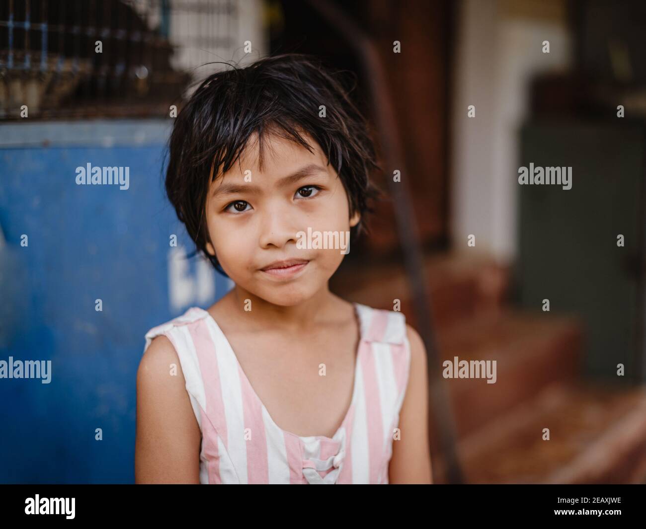 Portrait d'une jeune fille thaïe aux cheveux noirs courts, assise à l'extérieur de sa maison, regardant l'appareil photo. Banque D'Images