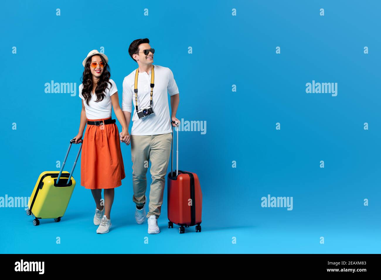 Un jeune couple heureux prêt à partir pour leurs vacances avec des valises colorées isolées sur fond bleu avec espace de copie Banque D'Images