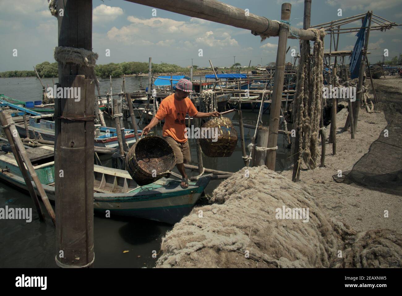 Un travailleur marchant sur un bateau après avoir lavé des paniers en rotin sur la plage d'atterrissage de Kamal Muara, un village de pêcheurs également connu sous le nom de centre de production de moules vertes dans la zone côtière de Jakarta, en Indonésie. Banque D'Images