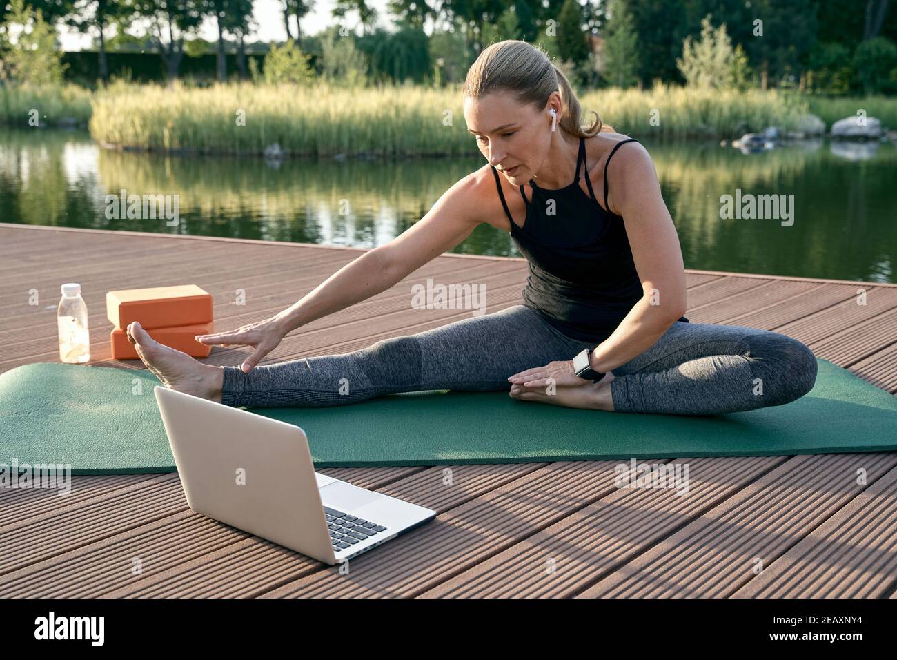 Pour votre paix intérieure. Femme sportive belle regardant le didacticiel sur un ordinateur portable tout en faisant du yoga sur un tapis dans la nature lors d'une journée ensoleillée à l'extérieur Banque D'Images