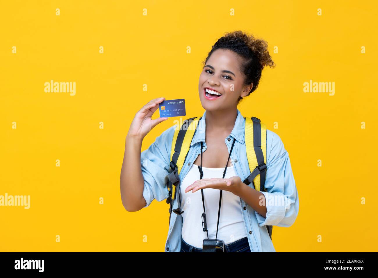 Bonne femme africaine américaine routard tenant une carte de crédit isolée dessus fond de studio jaune vif Banque D'Images