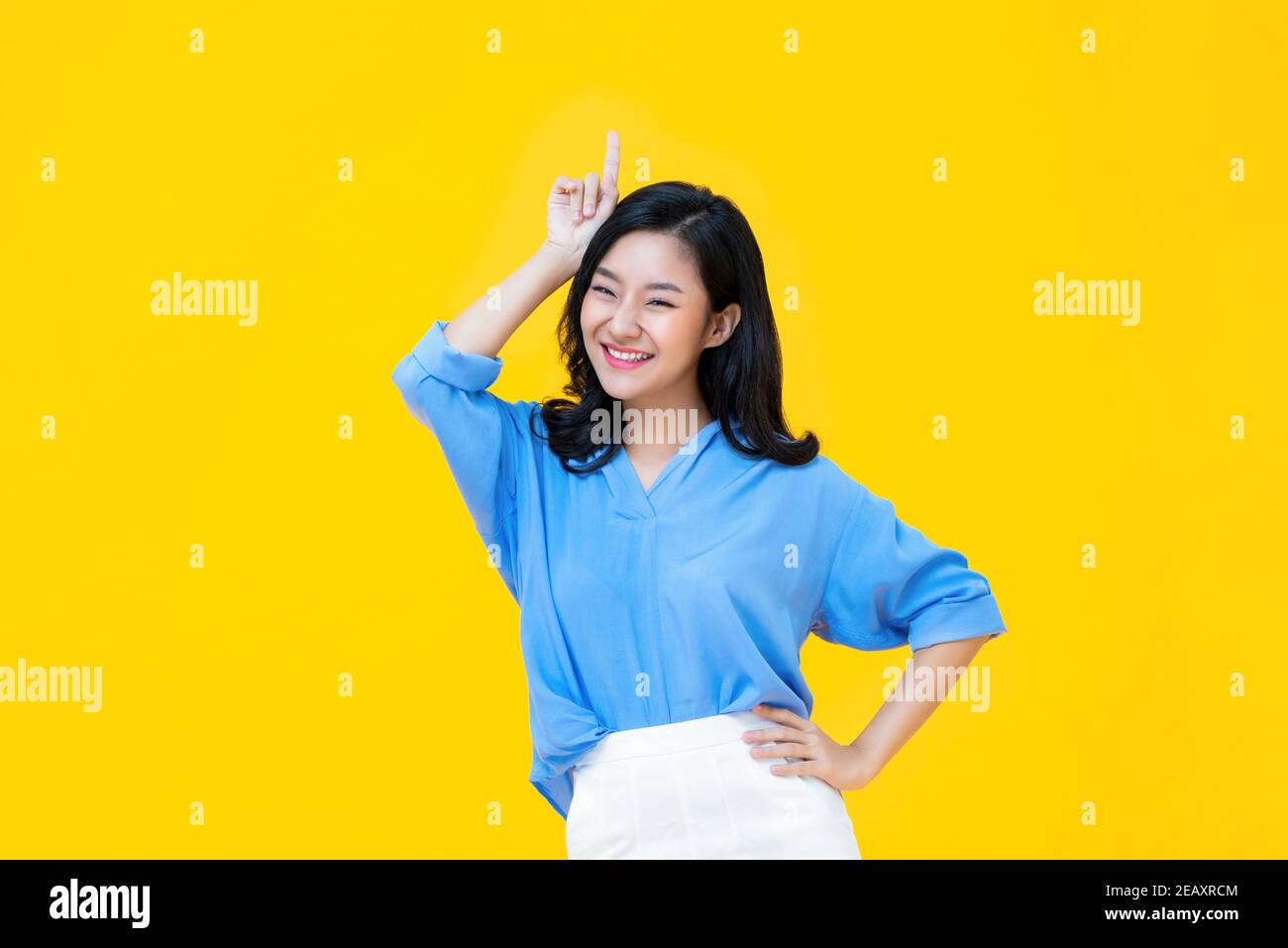 Jeune femme asiatique gaie dans des vêtements décontractés debout avec un main à la taille tandis que d'autres gesturing élevé elle est la meilleur sur fond jaune Banque D'Images