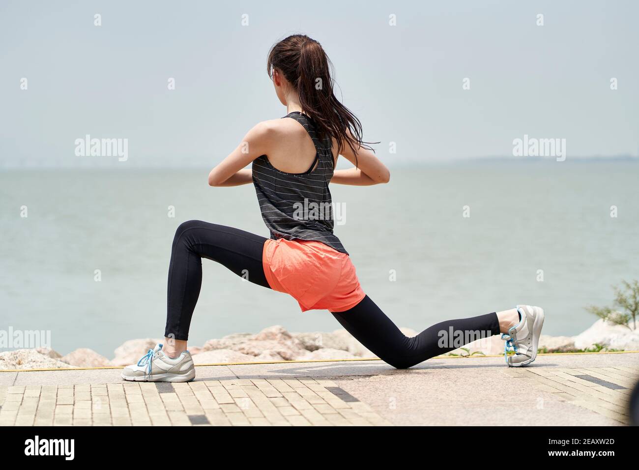 jeune femme asiatique en vêtements de sport s'échauffe avant de faire de l'exercice en plein air dans un parc en bord de mer Banque D'Images