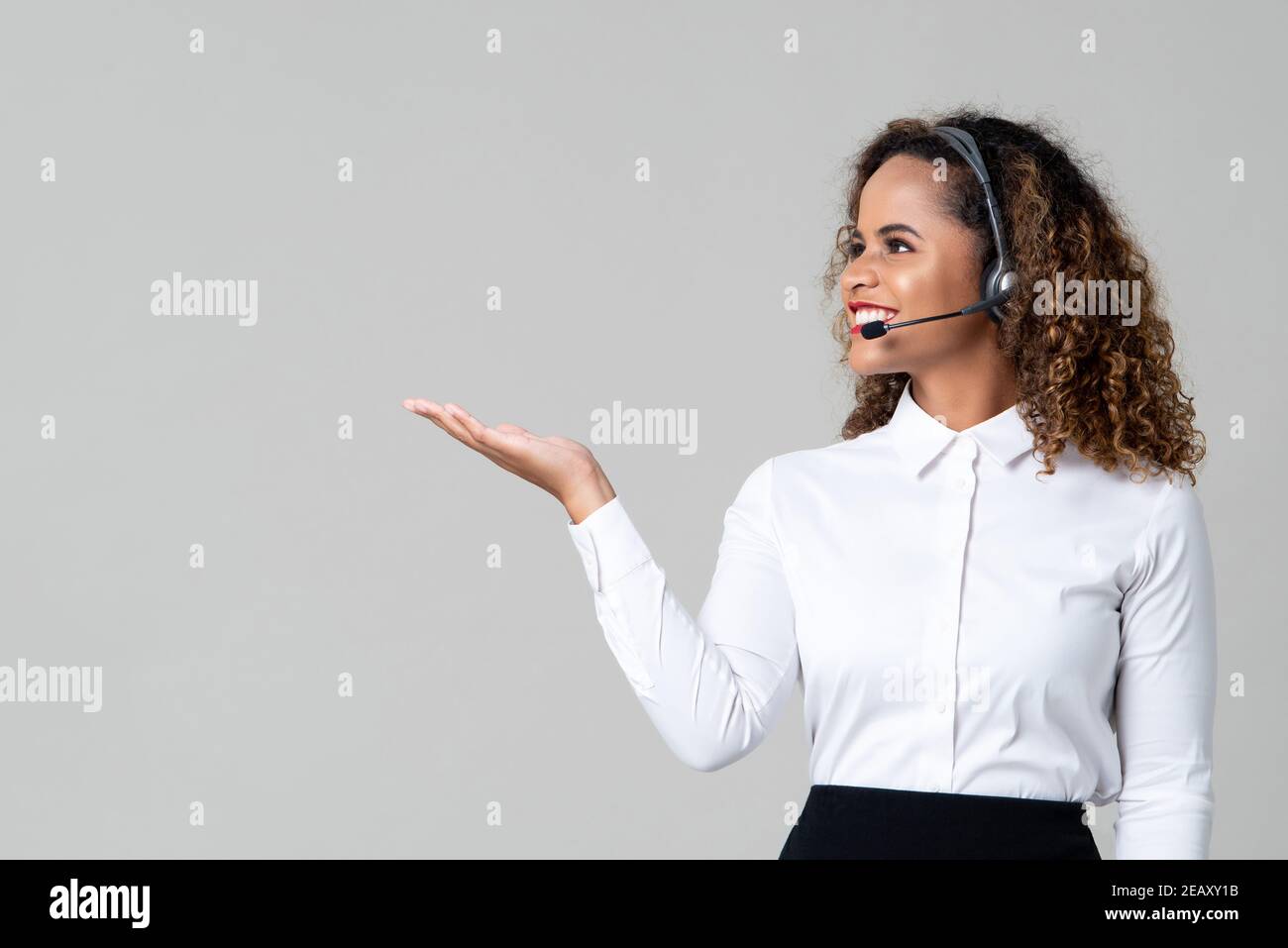 Service souriant femme afro-américaine sourit de porter des écouteurs personnel du centre d'appels avec main ouverte sur fond gris clair Banque D'Images