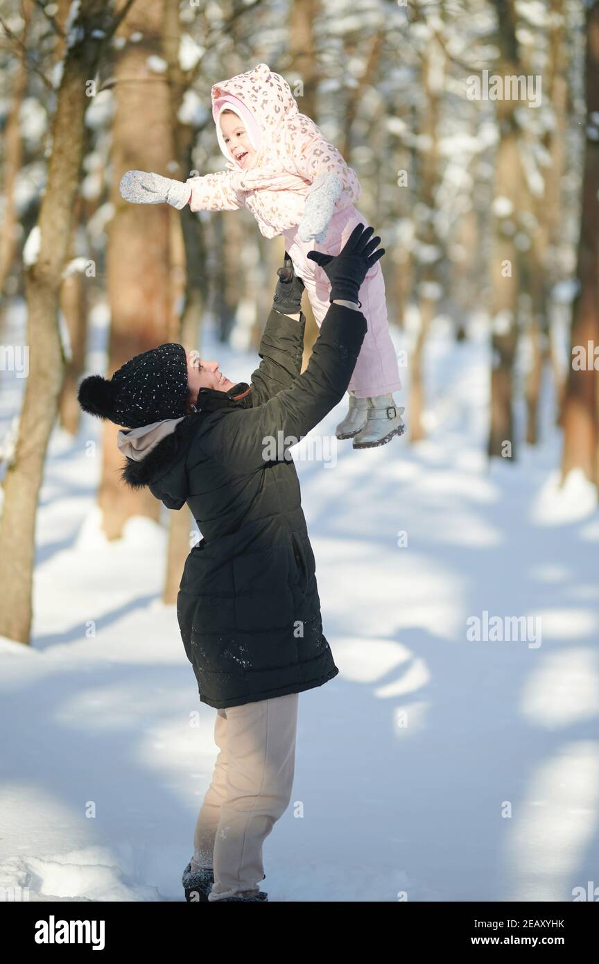 Maman lève sa fille sur fond de parc d'hiver Banque D'Images