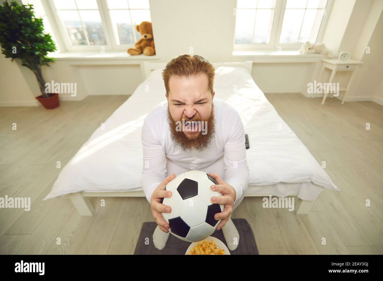 Drôle d'homme en pyjama blanc assis avec le ballon de football dedans les  mains sur le lit et crier Photo Stock - Alamy