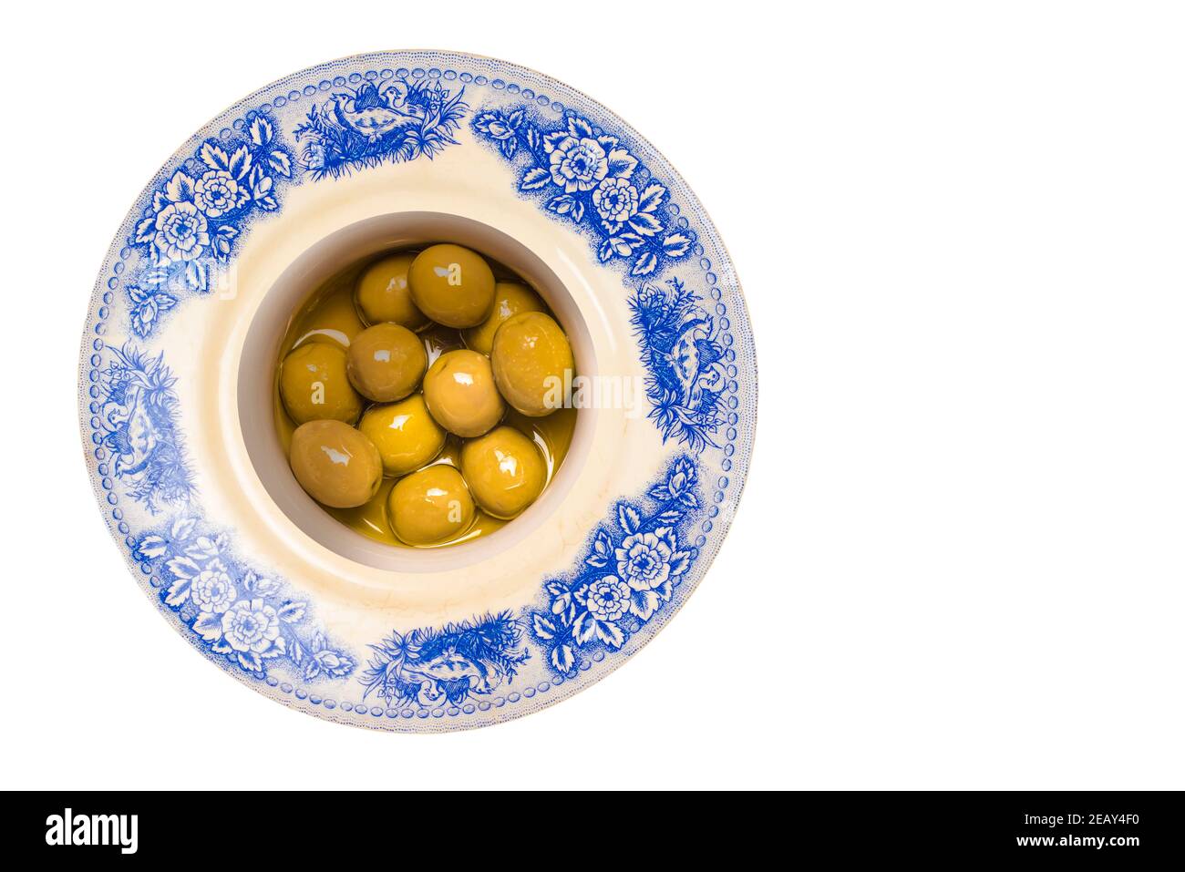 Olives vertes salées à l'huile d'olive dans une assiette vintage isolée sur fond blanc. Banque D'Images