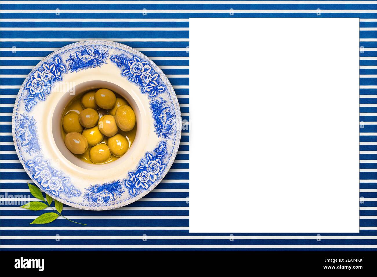 Olives sautées en os vert salé avec huile d'olive dans une assiette vintage sur une nappe doublée bleue et blanche et une feuille de papier vierge à écrire Banque D'Images