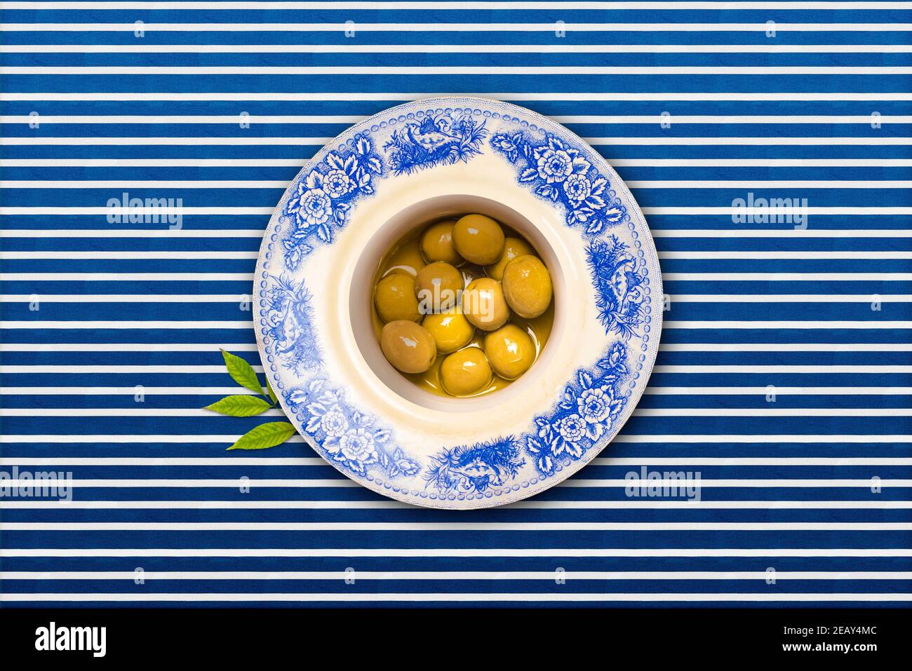 Olives vertes salées à l'huile d'olive dans un millésime assiette sur une nappe doublée bleue et blanche vue de ci-dessus Banque D'Images