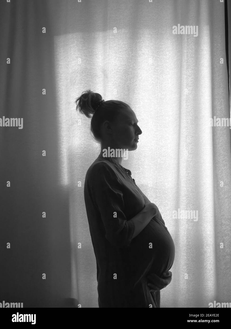 La silhouette d'une fille enceinte debout près de la fenêtre. Photo en noir et blanc. Banque D'Images