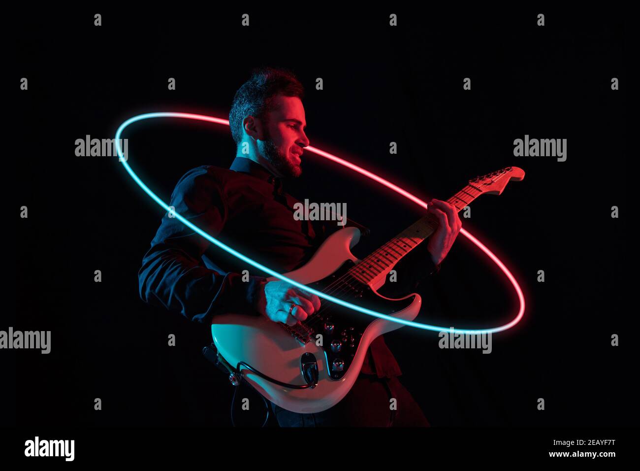 Jeune et joyeux musicien caucasien jouant de la guitare sur fond de studio  noir dans une lumière de néon avec un cercle futuriste lumineux néoné.  Concept de musique, passe-temps, festival. Portrait coloré