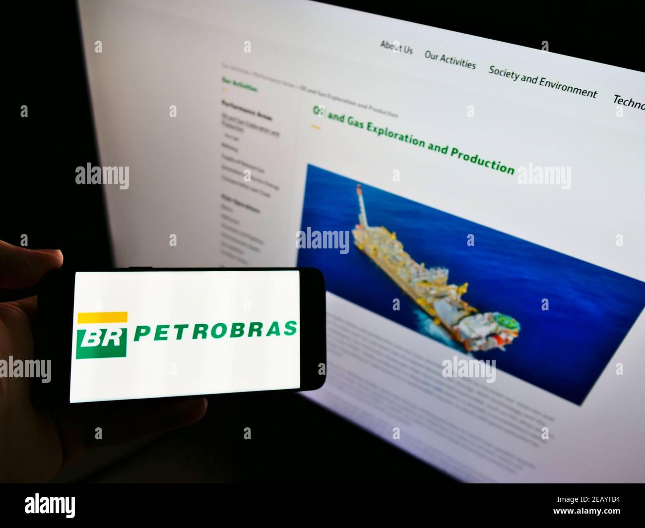 Personne tenant un smartphone avec le logo de la société pétrolière Petróleo Brasileiro S.A. (Petrobras) sur écran devant le site. Mise au point sur l'affichage du téléphone. Banque D'Images