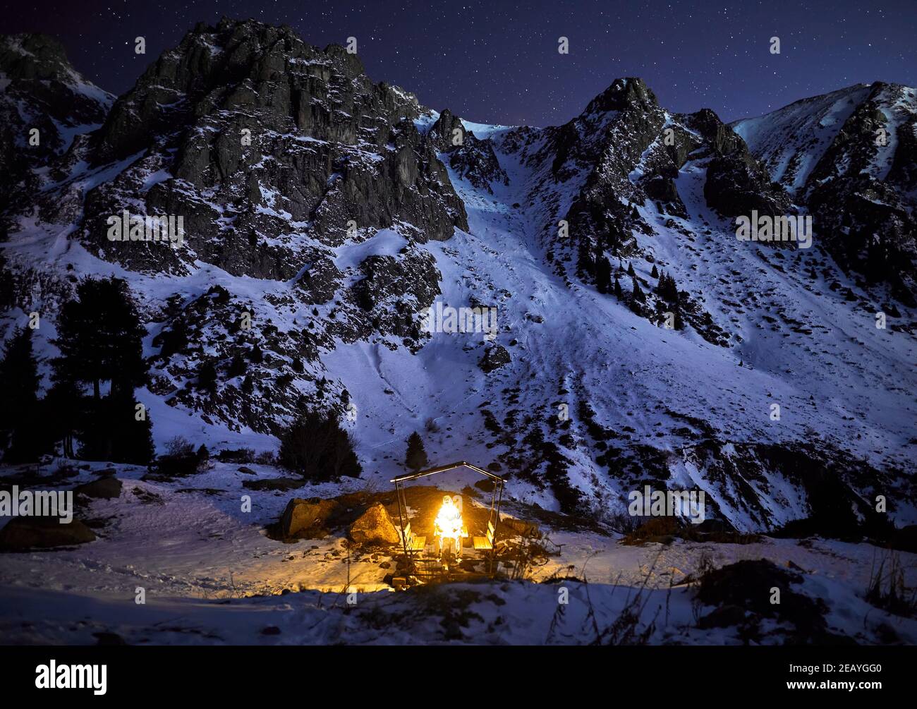 Homme avec guirlande orange lumineuse dans la maison en bois à montagnes d'hiver dans le ciel sombre Banque D'Images