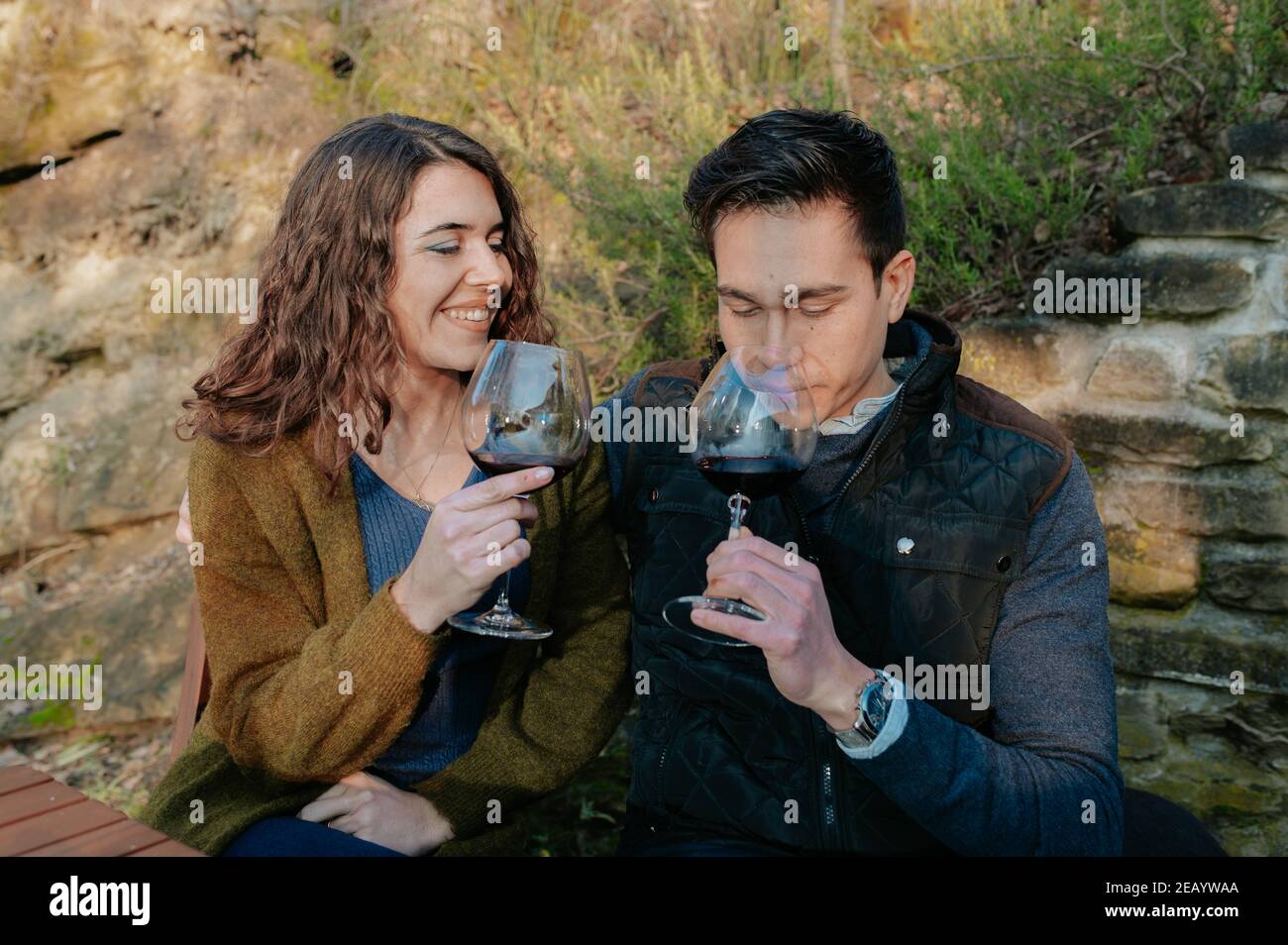 Jeune couple romantique assis dans un jardin et goûtant un verre de vin rouge pendant un pique-nique. Banque D'Images