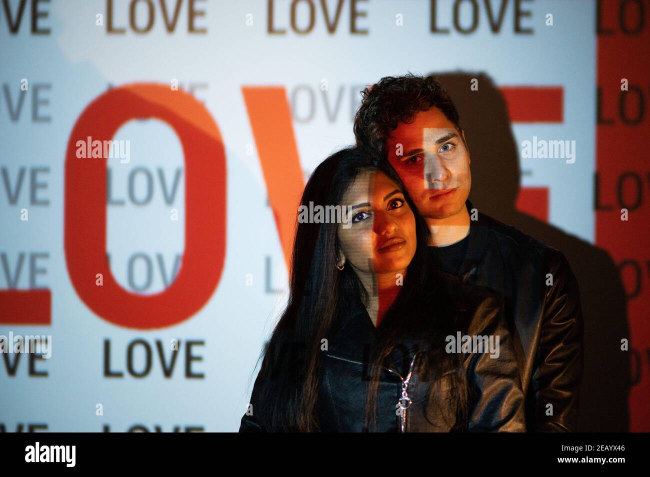 Couple Amerindien Et Caucasien Avec Veste Noire Regardant La Camera Les Amateurs De Studio Sombre Illumines Par La Lumiere Du Projecteur Avec Amour De Mot Photo Stock Alamy