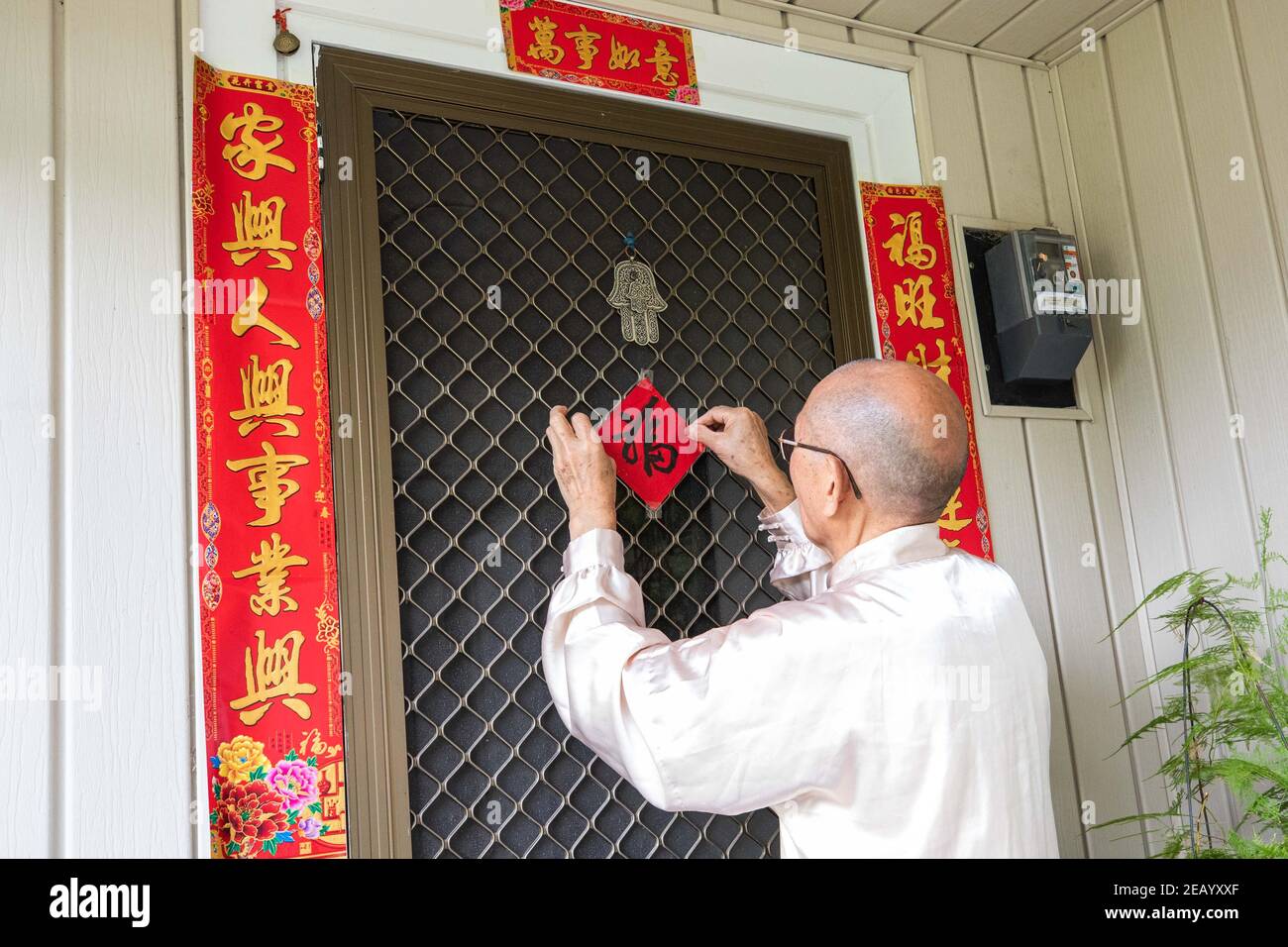 (210211) -- CANBERRA, 11 février 2021 (Xinhua) -- Huang Yiquan pâtes couplets couplets et le caractère chinois Fu, ce qui signifie bénédiction, sur une porte pour célébrer le nouvel an chinois à Canberra, en Australie, 9 février 2021. Fabrication de boulettes, mise en place de couplets, danse traditionnelle... les Chinois de Canberra, capitale australienne, trouvent différentes façons de créer une atmosphère pour le Festival du printemps. POUR ALLER AVEC le « nouvel an chinois célébré dans la capitale australienne avec des boulettes, des couplets et des souhaits de retourner bientôt en Chine » (photo de Chu Chen/Xinhua) Banque D'Images