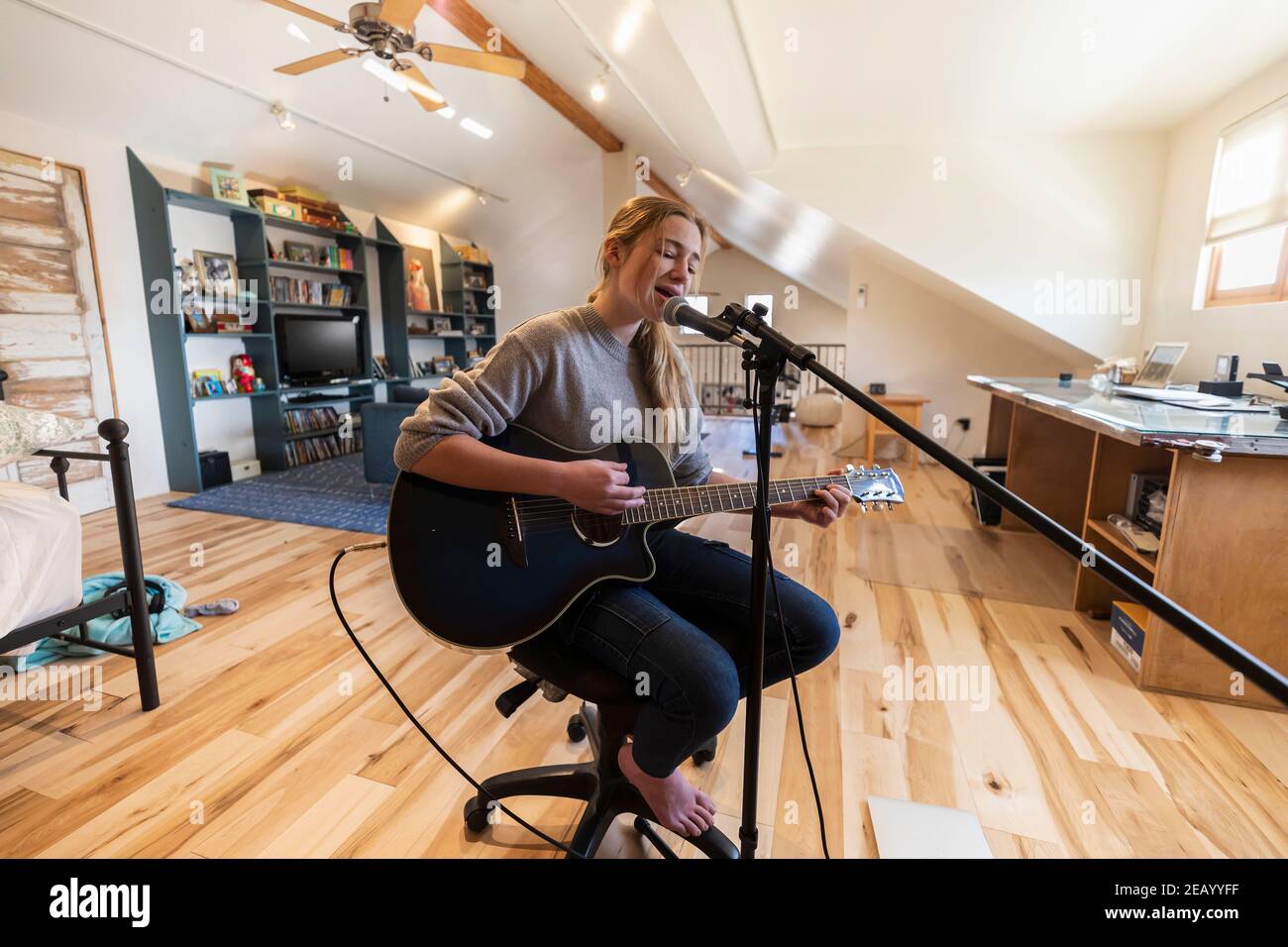 Adolescente de quatorze ans jouant sa guitare et chantant à la maison dans l'espace loft Banque D'Images