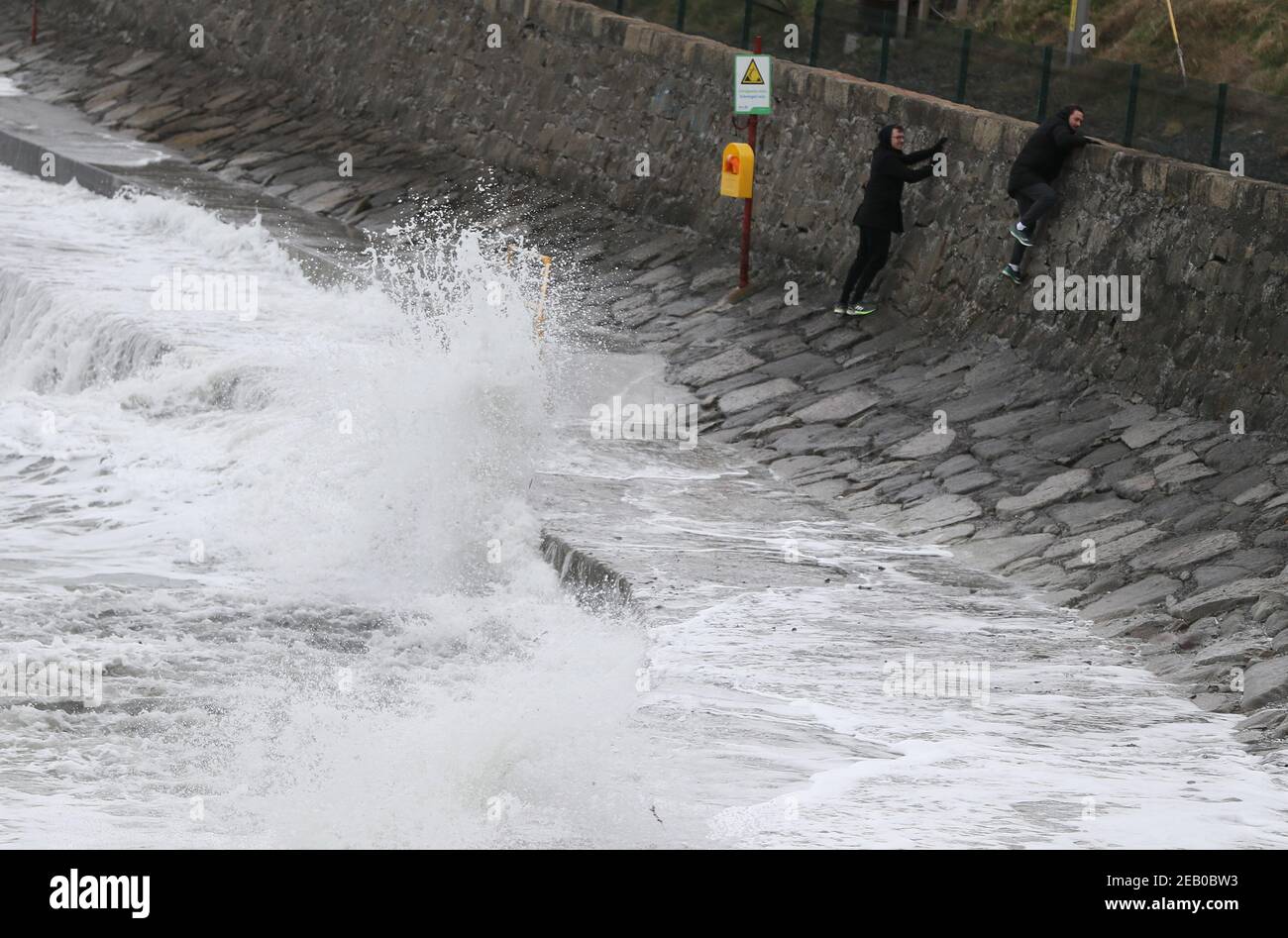 Deux hommes escaladent un mur pour éviter de briser les vagues le long du front de mer à Seapoint Beach à Dublin comme met Eireann ont émis deux avertissements météorologiques, y compris des vents forts à gales du sud-est en conjonction avec la pluie, la grésil et la neige. Date de la photo : jeudi 11 février 2021. Banque D'Images