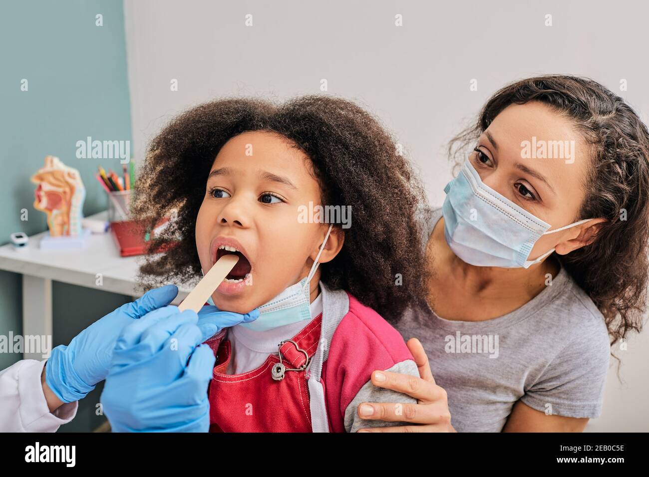 Docteur utilisant la spatule d'inspection pour examiner la gorge d'une fille afro-américaine. Petite fille avec sa mère au rendez-vous pédiatre Banque D'Images