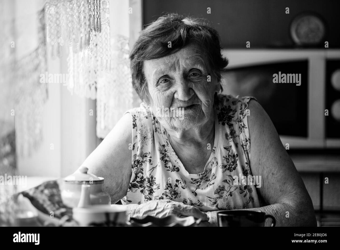 La vieille femme pensionnée est assise à une table dans sa maison. Photo en noir et blanc. Banque D'Images