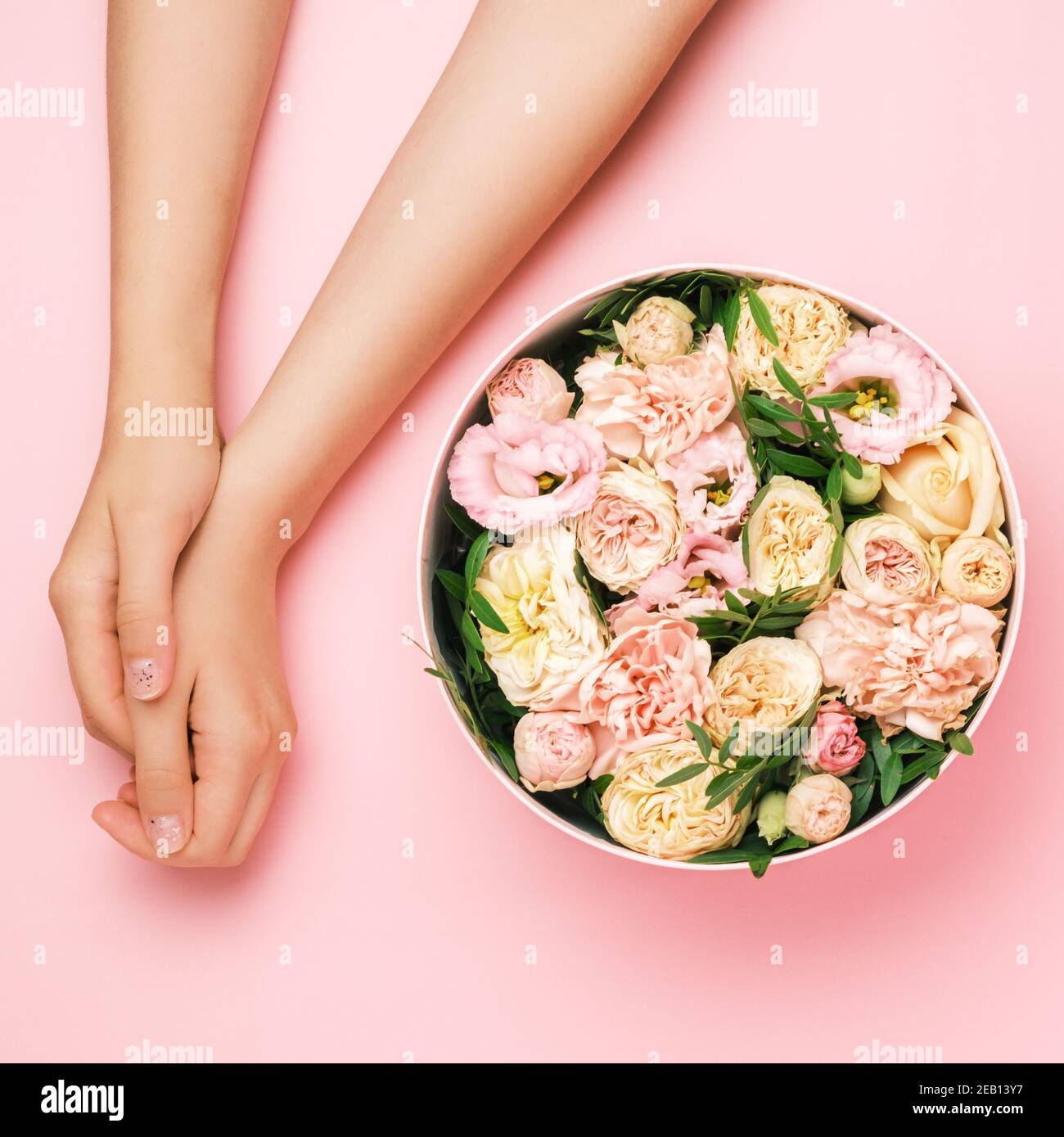 Boîte avec de belles fleurs à côté des mains de womans sur le fond noir avec espace de copie. Concept de carte salone beauté. Cadeau pour le 8 mars, Fête des mères Banque D'Images