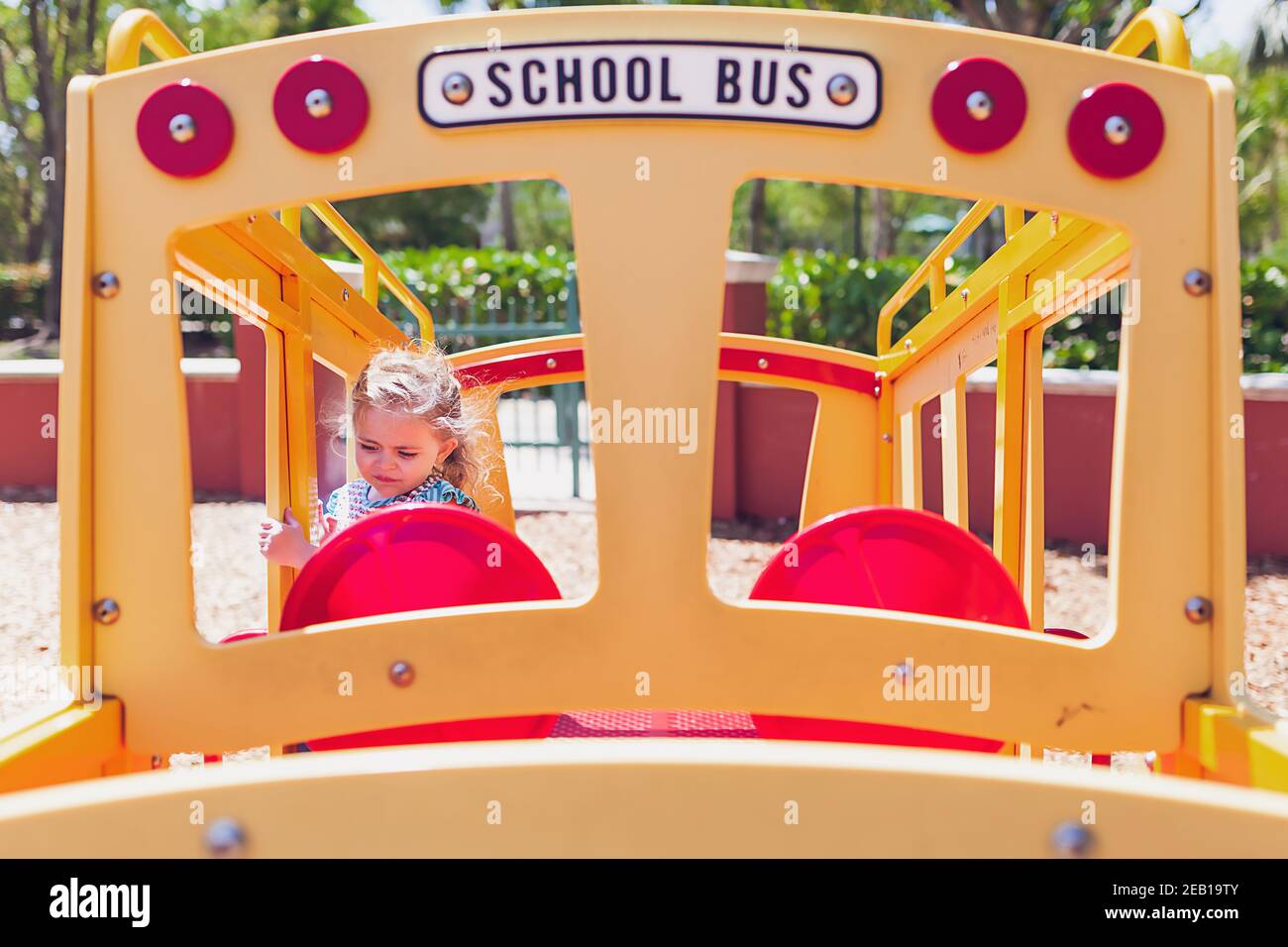 Petite fille jouant sur un jouet d'autobus scolaire dans une aire de jeux. Banque D'Images