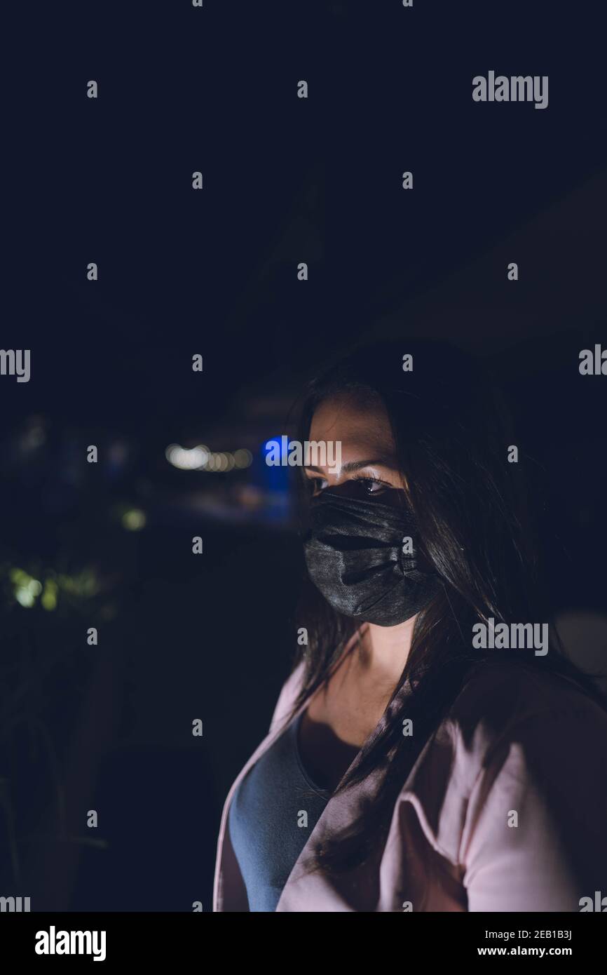 Femme portant le masque de sécurité du visage son visage illuminé portant un masque contre le coronavirus, rue sans personnes à l'arrière-plan Banque D'Images