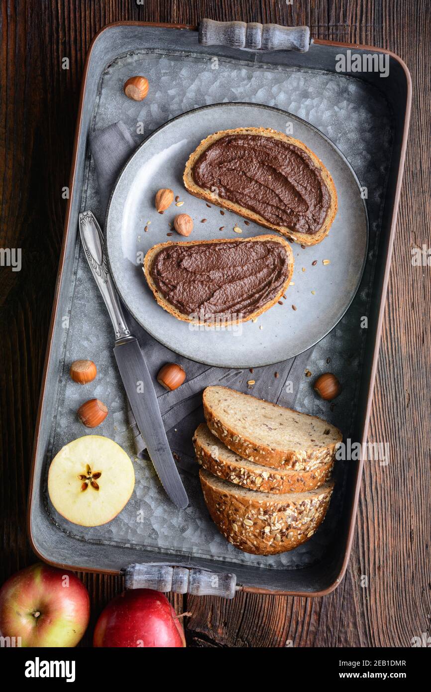 Petit déjeuner sain, tranches de pain aux grains entiers avec tartinade aux pommes en poudre de cacao, noisettes grillées et chocolat noir sur bois rustique Banque D'Images