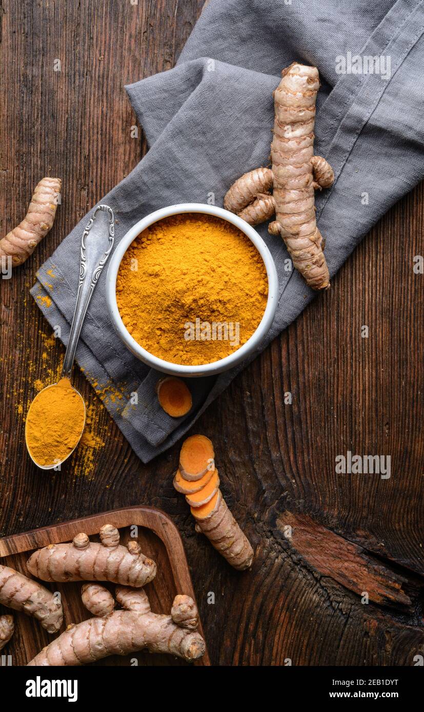 Ingrédient alimentaire anti-inflammatoire, poudre de curcuma dans un bol en céramique et racine fraîche sur fond rustique en bois Banque D'Images
