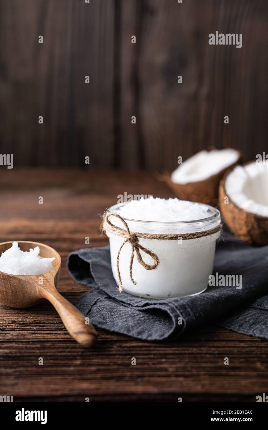 Huile de noix de coco bio pressée à froid super-alimentaire dans un pot en verre, décorée de noix fraîches sur fond de bois rustique avec espace copie Banque D'Images