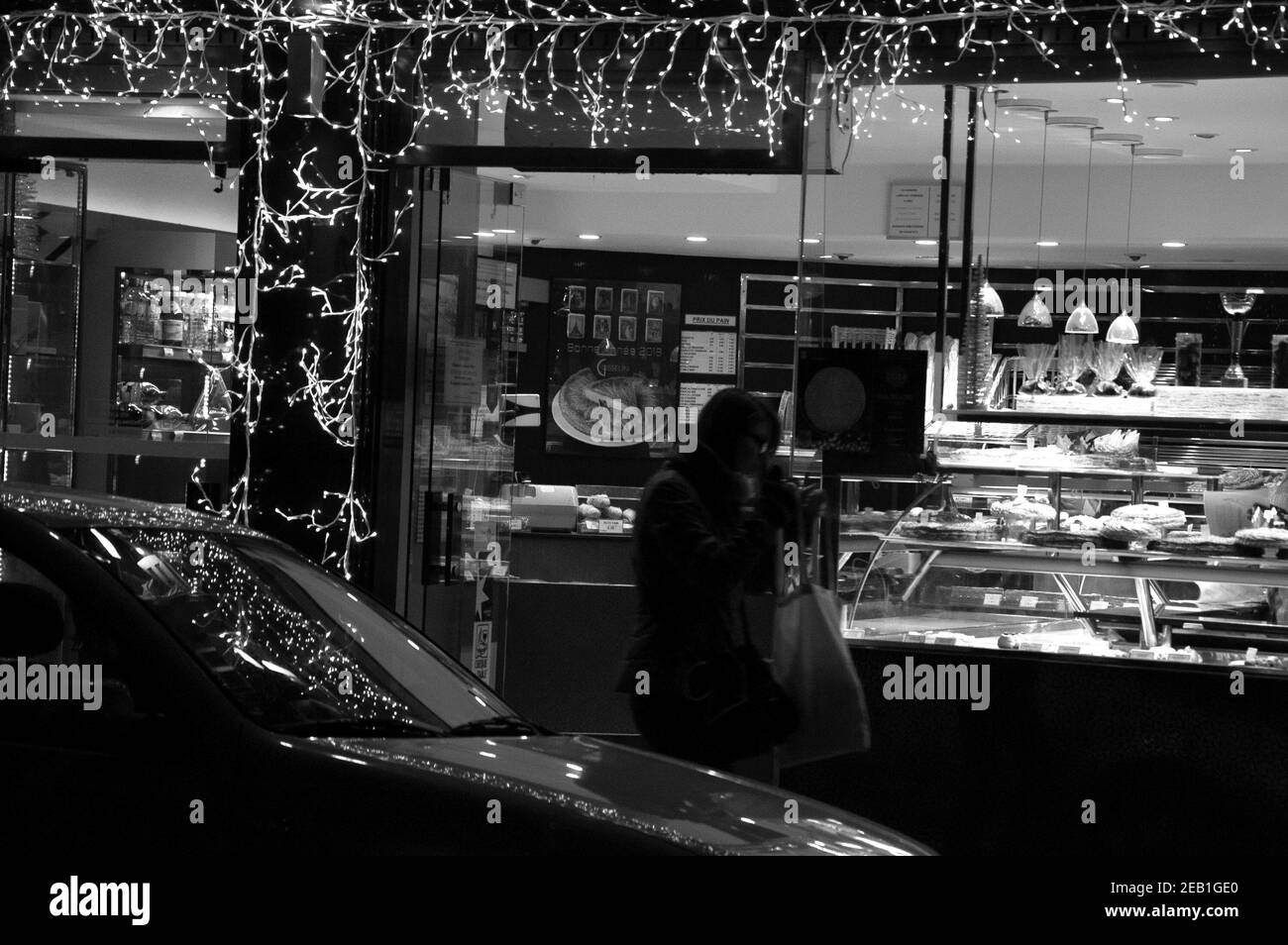 Femme sortant de la boulangerie parisienne décorée de guirlande lumineuse pour les vacances d'hiver. Paris, France. Photo historique noir blanc Banque D'Images